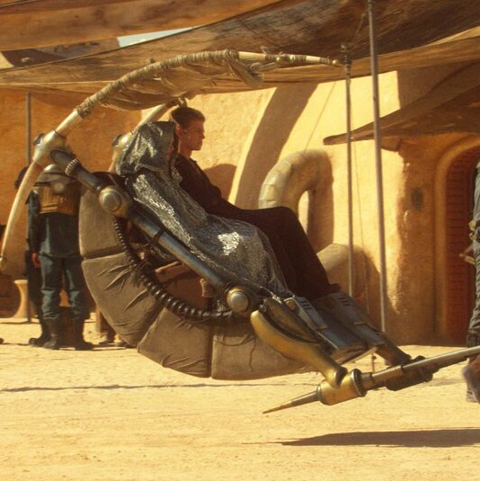 Two humans riding a carriage through the busy streets of Tatooine