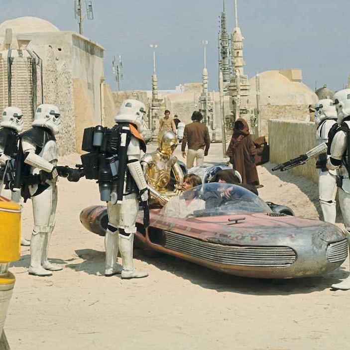 A group of stormtroopers running a checkpoint with a speeder